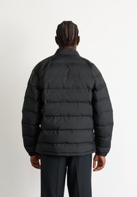 Schwarze Daunenjacke mit dicken horizontalen Steppabschnitten, einem Stehkragen und elastischen Bündchen, die für Wärme ausgelegt ist.