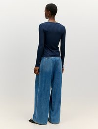 Navy ribbelde Langarmshirt mit rundem Ausschnitt, kombiniert mit weit geschnittenen hellblauen Jeans aus Denim, die sichtbare Nähte aufweisen und einen lässigen Sitz haben.
