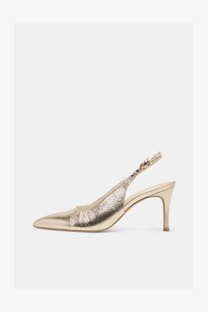 Zapato de tacón alto con punta afilada y tira trasera tipo slingback en color dorado metálico, con un tacón delgado de altura media y una correa ajustable con hebilla.