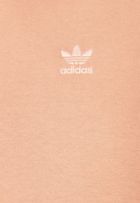 Pomerančově zbarvená pletenina s bílým vyšívaným logem Adidas trefoil na levé straně. Hladký povrch s žebrovaným vzorem.