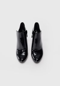 Paire de bottines en cuir noir brillant avec bouts pointus, fermeture éclair latérale et marquages de taille 37 à l'intérieur, vues de dessus sur fond gris.