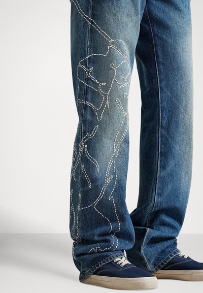 Zilas džinsa bikses ar baltu izšuvumu gar kāju. Klasisks taisns piegriezums ar nodilušu faktūru. Kombinēts ar tumši ziliem sporta apaviem.