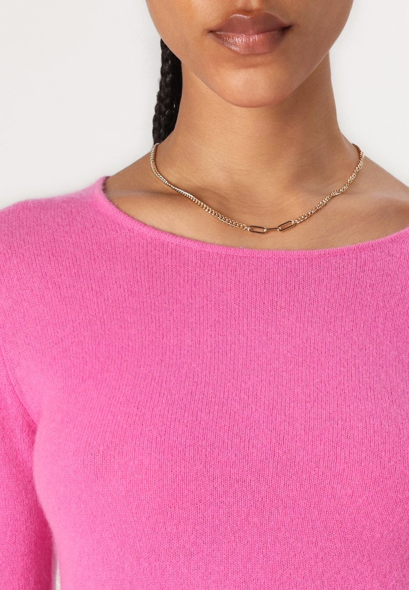 Rosa Strickpullover mit rundem Halsausschnitt, aus weichem Material gefertigt. Eine goldene Kettenhalskette mit kleinen ovalen Gliedern liegt am Schlüsselbein.
