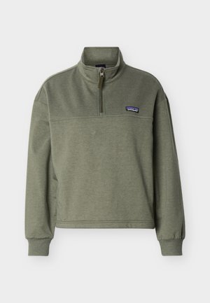 Polaire Patagonia couleur vert olive, modèle pull-over avec fermeture éclair au quart, col montant, poignets côtelés, et petite écusson logo sur la poitrine gauche.