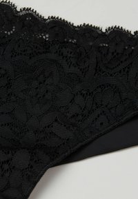 Lingerie in pizzo nero con motivi floreali intricati, texture del tessuto morbida e bordo nero solido lungo i contorni.