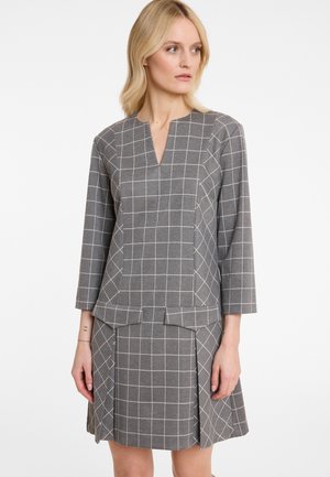 Robe à carreaux grise avec un décolleté en V et des manches trois quarts. Le tissu présente un motif de grille avec un corsage ajusté et une jupe évasée.