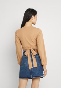 Top castanho canelado de manga longa com um laço nas costas, combinado com uma mini saia de ganga azul com bainha desfiada e bolsos.