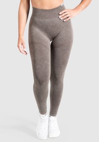 Leggings marroni a vita alta realizzati in un materiale morbido ed elastico, con dettagli texture e una finitura liscia, abbinati a sneakers bianche.