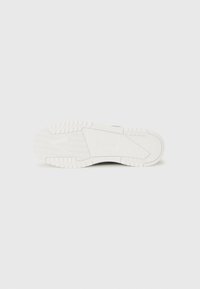White sneaker sole with rubber material, textured grip, and patterned tread. Features logo detail and a contoured design for comfort.