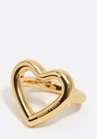 Złoty pierścionek w kształcie serca z gładkim, polerowanym wykończeniem; posiada otwarty środek oraz obrączkę z wygrawerowanym napisem "BIMBA Y LOLA".