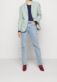 Ljusgrön kavaj, marinblå topp, högmidjade ljusblå jeans och spetsiga bordeauxfärgade klackar. Kavajen har en enkel knapp och en strukturerad passform.