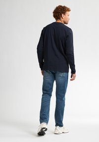 Maglietta a maniche lunghe di colore blu navy abbinata a jeans azzurri e sneakers bianche. Presenta un design semplice con scollo rotondo e vestibilità comoda.
