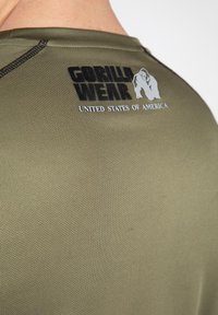Olijfgroene sportshirt met een textuur, ronde halslijn en een bedrukte logo met "GORILLA WEAR" en "VEREENIGDE STATEN VAN AMERIKA."