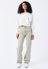 Felpa bianca cropped con piccolo logo ricamato, abbinata a jeans verde chiaro a vita alta con taglio dritto e leggere sfumature.