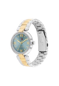 Reloj de metal en tonos plata y dorado con una caja redonda, esfera azul, números romanos y un bisel engastado de cristales. Cuenta con un cierre.