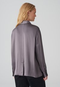 Zijdeachtige, lichtgrijze shirt met een klassieke kraag, lange mouwen en knoopsluitingen bij de manchetten. Beschikt over een middelste rugnaad en een relaxte pasvorm.