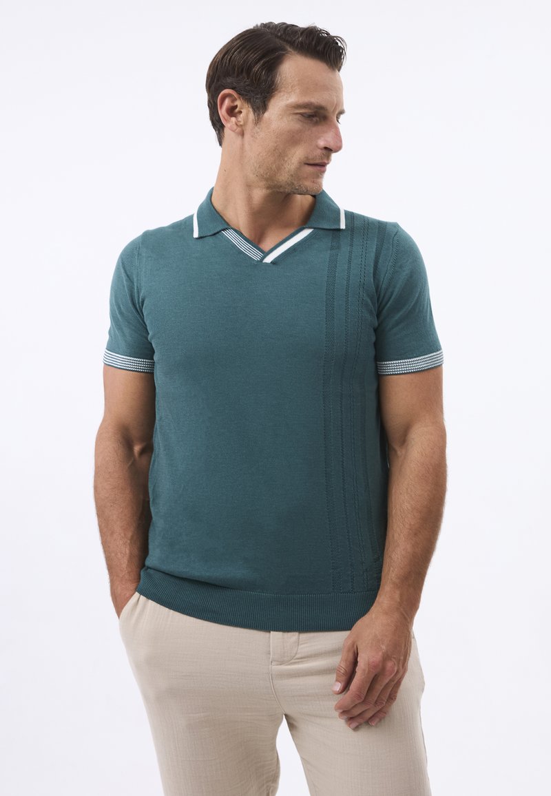 Teal värvi kudum polo-särk valge krae ja mansettidega. Ühel küljel on vertikaalne tekstuurimuster, slim fit lõige ja lühikesed varrukad. Sobitatud beežide pükstega.