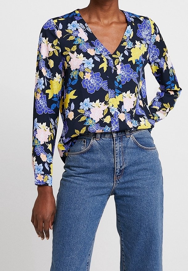 Květinová blůza v námořnické modři s dlouhými rukávy, zdobená modrými, růžovými a žlutými květinami. V-čkový výstřih, doplněná vysokými modrými džíny.