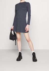 Grå långärmad klänning med figursydd överdel, utsvängd kjol och detalj med mittsöm, i kombination med svarta ankelboots och en liten svart väska.