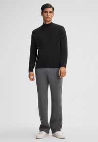 Maglione nero a collo alto in maglia con un motivo testurizzato, abbinato a pantaloni della tuta grigi con cuciture laterali a contrasto e sneakers bianche.