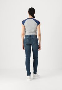 Camiseta gris ajustada con mangas en azul marino, combinada con unos jeans ajustados de color azul oscuro. Unos zapatillas blancas completan el atuendo.