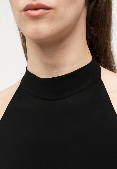 Γυναίκα με μαύρο αμάνικο τοπ halter που δείχνει το ντεκολτέ και το κάτω μέρος του προσώπου με φυσικά χείλη και μακριά καστανά μαλλιά πίσω από τους ώμους.