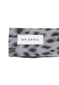 Tissu gris avec un motif léopard noir, comportant une étiquette blanche rectangulaire sur laquelle est inscrit "OH APRIL" en texte noir.