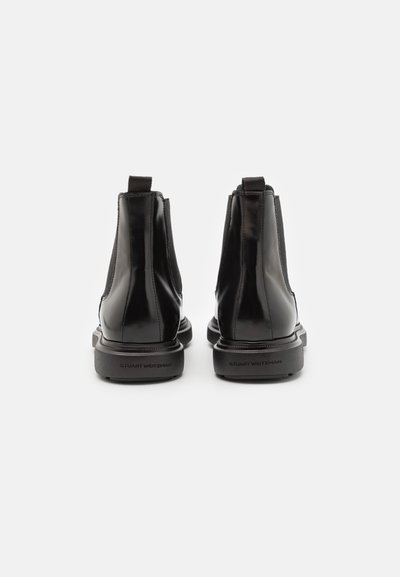 Botas de tobillo de cuero negro con un acabado brillante, paneles elásticos en los laterales y una suela plana de goma. Logo impreso en el talón.