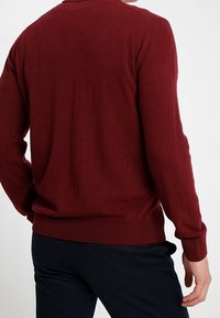 Burgundowa sweter wykonany z miękkiego materiału, z okrągłym dekoltem oraz ściągaczami przy mankietach i u dołu. Charakteryzuje się gładką fakturą i dopasowanym fasonem.