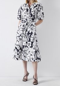 Blommönstrad klänning med krage, korta puffärmar, midjebälte och knälång kjol i svart och vitt.