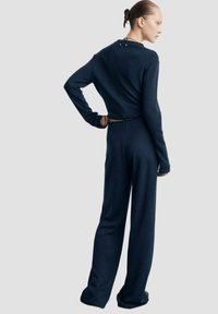 Combineu de culoare albastru marin, cu mâneci lungi, având un top mulat și pantaloni largi, cu talie ajustată și o închidere la spate. Textură moale.