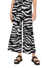 Pantalons larges à imprimé zèbre noir et blanc avec une finition texturée et une taille élastique, associés à des sandales noires chunky.
