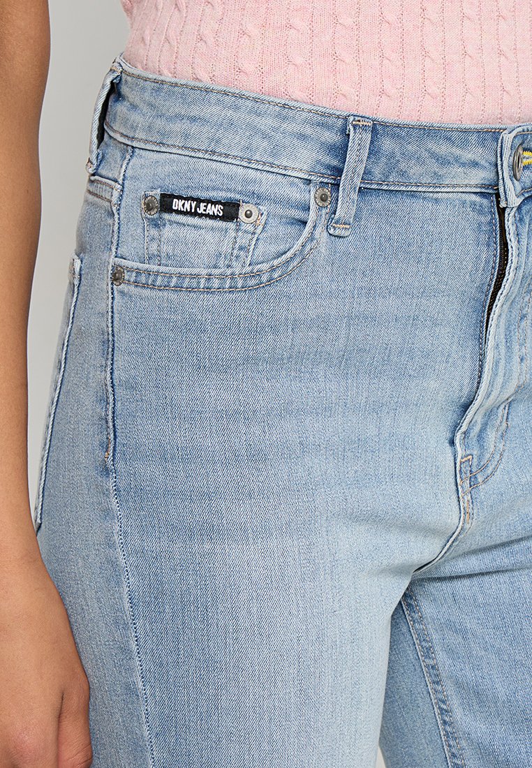 Jasnoniebieskie dżinsy o dopasowanym kroju. Cechy obejmują czarną metkę z napisem "DKNY JEANS", przednie kieszenie i subtelne szczegóły przeszyć.