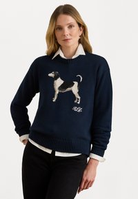 Marineblauwe trui met een ronde hals, voorzien van een gebreid hondenontwerp in zwart, wit en beige aan de voorkant, met ribbels aan de manchetten en de onderkant.