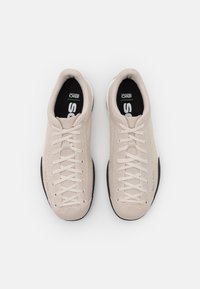 Baskets beiges avec une tige en mesh texturé, une semelle extérieure en caoutchouc noir et des lacets, avec un col et une languette rembourrés pour plus de confort.