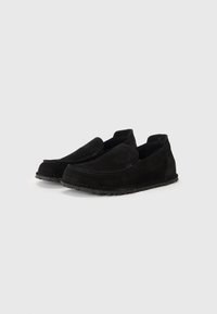 Sorte semskede slip-on sko med lav profil, rund tå og teksturert gummisåle. Har minimalt med søm og ingen synlig maskinvare.