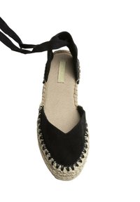 Espadrille de lona negra con puntera en forma de V y suela de yute trenzado, que presenta acentos de costura negra y largas cintas de tela para un ajuste seguro.