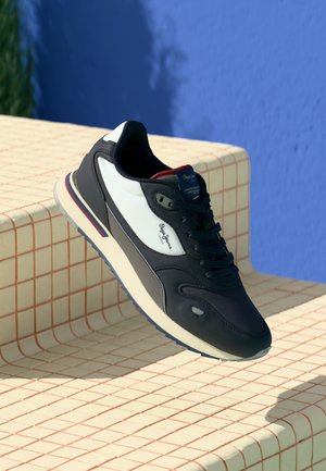 Men's sneaker featuring a black leather upper with white and grey accents, round toe, lace-up front, and rubber sole with a striped detail.