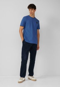 Niebieska bawełniana koszulka z krótkim rękawem, okrągłym dekoltem i małym logo na lewej piersi. W połączeniu z granatowymi spodniami z korduroy i białymi sneakersami.