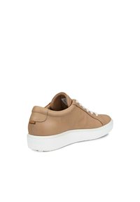 Beige lädersneaker med vit gummisula, rund tå och platta vita snören. Har en sydd design och en liten accent vid hälen.