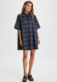 Blå och svart rutigt oversized skjortklänning med korta ärmar, krage och mjukt tyg, i kombination med svarta platåskor.