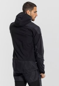 Giacca nera con cappuccio dal finitura liscia e opaca. Presenta pannelli a contrasto, una vestibilità rilassata e corde regolabili sul cappuccio.