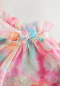 Tissu transparent à volants dans des couleurs pastel arc-en-ciel avec une texture fine en maille, rassemblé à une couture sur un vêtement de couleur claire.