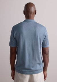 Jasnoniebieska koszulka polo z krótkimi rękawami, posiadająca teksturowany wzór dzianiny na ramionach. Miękki materiał, luźny krój, prążkowany kołnierzyk i mankiety.