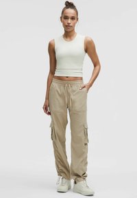 Beżowe spodnie cargo z wieloma bocznymi kieszeniami, elastycznymi mankietami i sznurkiem w talii, w połączeniu z dopasowaną, jasnoskalną bluzką bez rękawów.