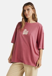 Oversized berry-pink cotton t-shirt with short sleeves and round neck. Features a white logo printed on the front, smooth texture.