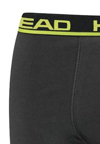 Schwarze Boxershorts mit breitem elastischem Bund, in dem "HEAD" in leuchtendem Gelb aufgedruckt ist. Der Stoff wirkt glatt mit feinen Nähdetails.