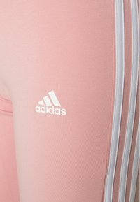 Rosa leggins i stretchy tyg, med tre vita ränder längs sidan och en liten vit Adidas-logotyp på låret.