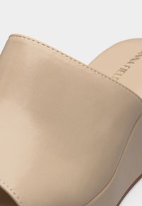 Μπεζ δερμάτινο mule με καστόνι, ψηλό χοντρό τακούνι, ραμμένο άνω μέρος και ορατό όνομα μάρκας στη σόλα εσωτερικά.