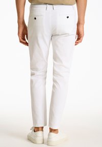 Białe bawełniane spodnie o wąskim kroju, z tylnymi kieszeniami zapinanymi na czarne guziki oraz prostymi nogawkami. Noszone z białymi trampkami.